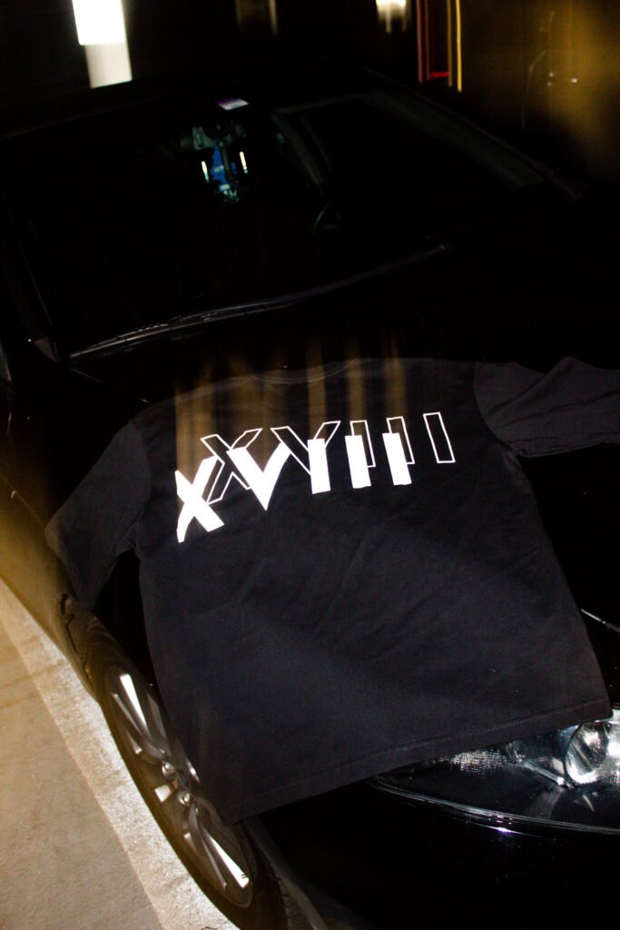 Black EXACTITUDE brand oversized t-shirt displayed on a black car with roman Numeral in the back. Product image.